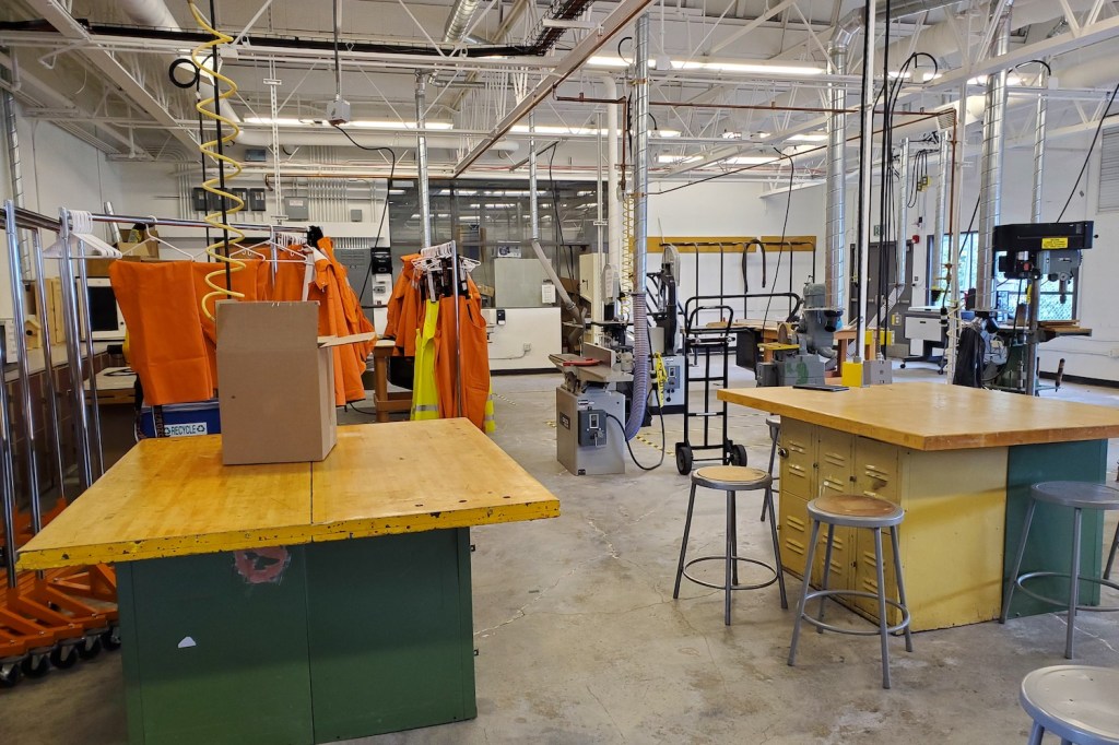 A room with tables, woodworking equipment and orange foul weather gear.