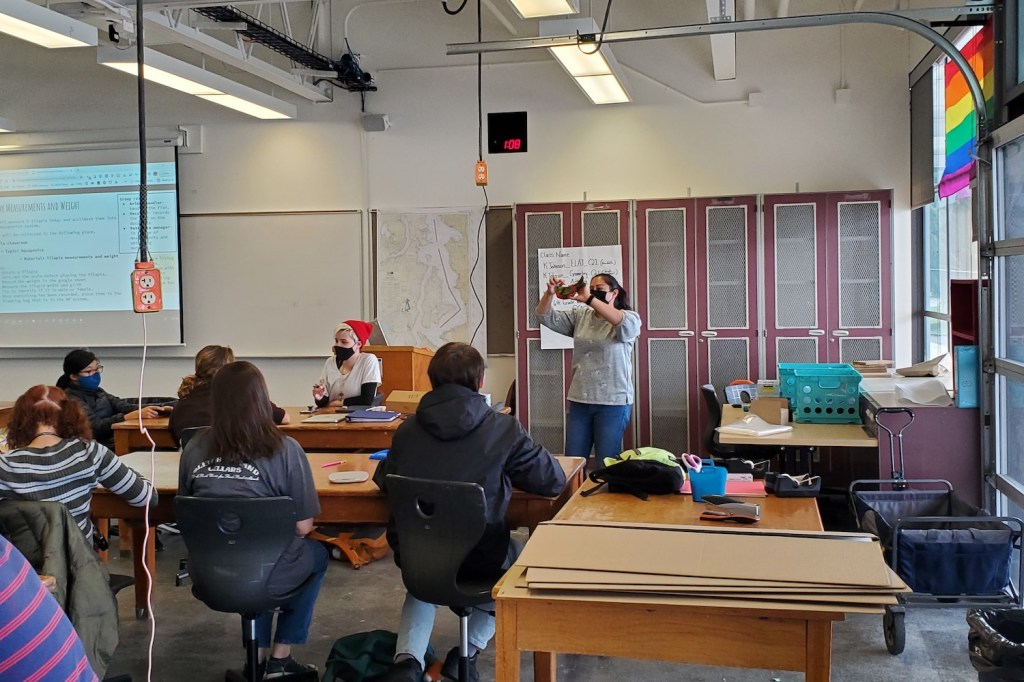 A teacher holds up a stuffed fish as part of a demonstration in front of students.