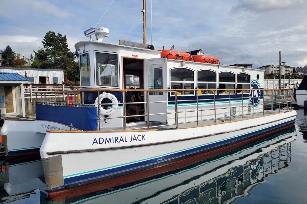 A boat with two hulls is at the dock, inside the cabin students are seated wearing lifejackets